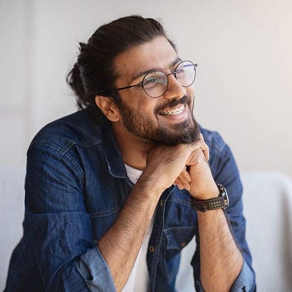 Smiling man with round glasses and a beard, wearing a denim shirt, resting his chin on his hands.