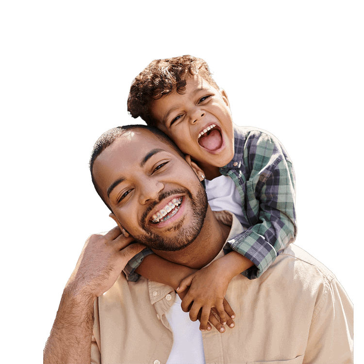 Adult man smiling with braces, carrying a laughing child on his shoulders, both looking joyful.